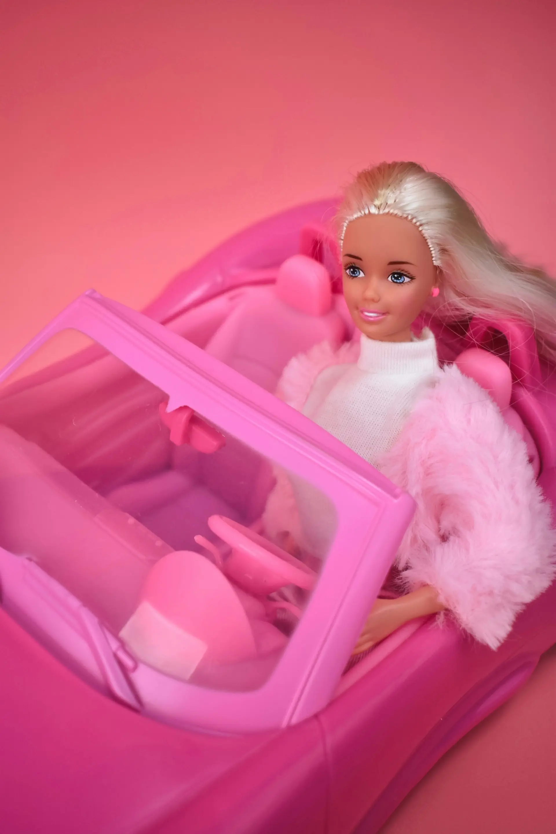 A Barbie doll sitting in a pink toy convertible